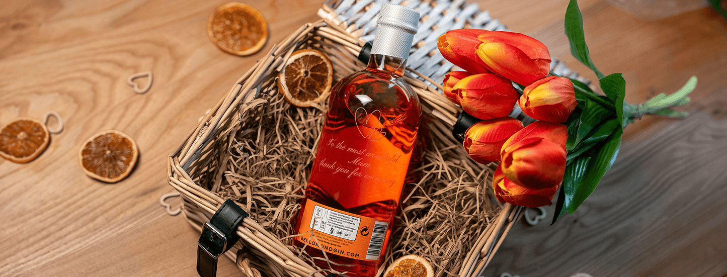 Bottle of alcohol in a woven basket with dried oranges and tulips on a wooden surface