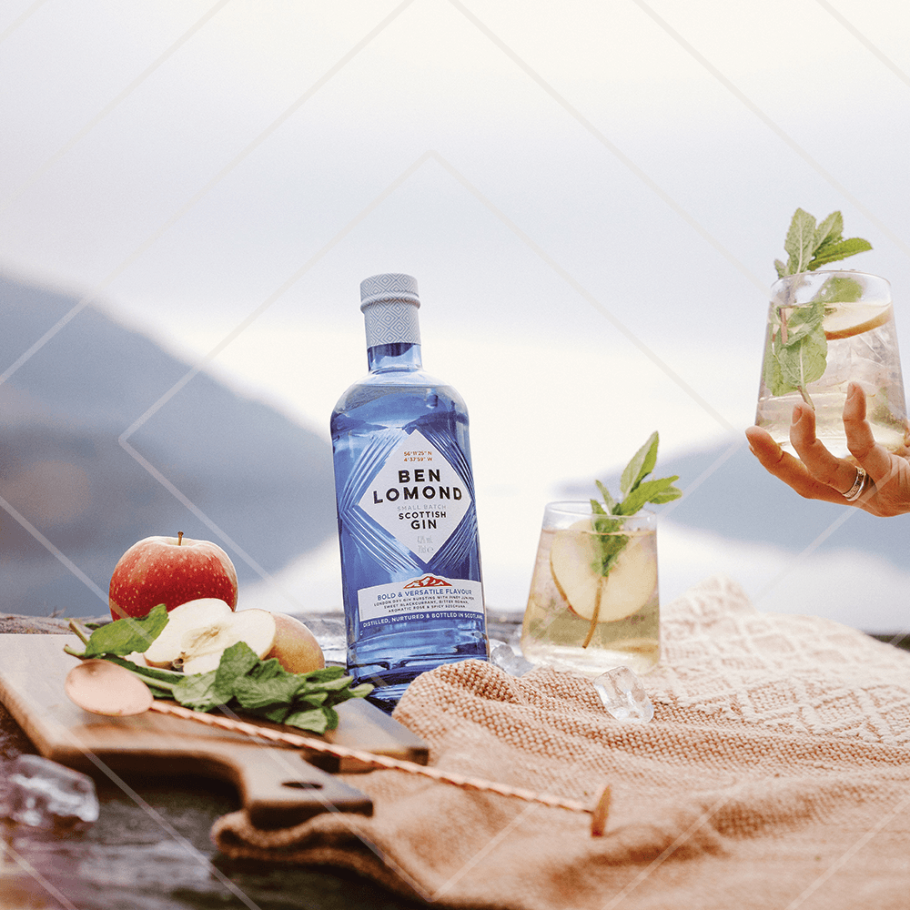 Bottle of Ben Lomond Scottish Gin with a glass of gin and tonic on a table with apples and herbs.