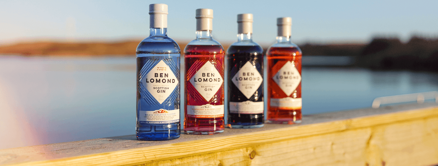 Four bottles of Ben Lomond gin on a wooden surface with a scenic background