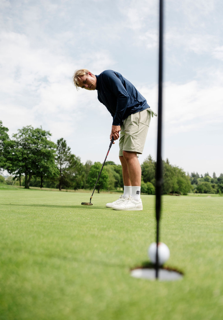 Man playing golf on a green course with trees in the background