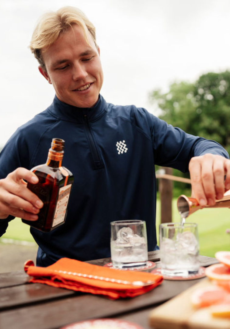 Man pouring a drink from a bottle into a glass at an outdoor setting