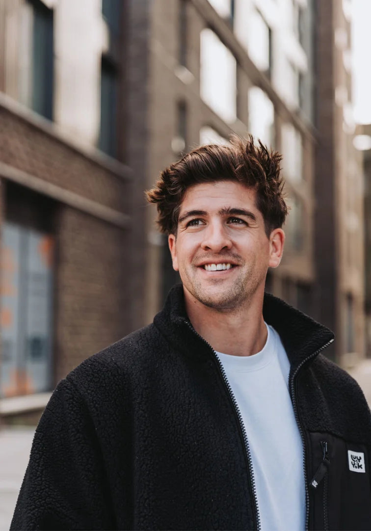 Man smiling outdoors with blurred buildings in the background