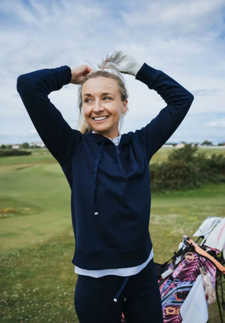 Woman on a golf course with a blue jacket and white shirt, smiling.