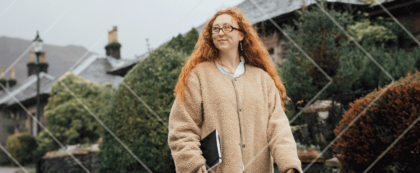 Person with red hair wearing a beige sweater standing outdoors with a blurred background